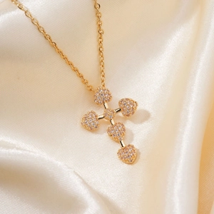 Macro shot of gold-plated heart-shaped cross pendant with crystals on champagne satin