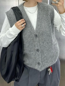 Dettaglio del gilet in maglia grigio con scollo a V e bottoni indossato dal modello
