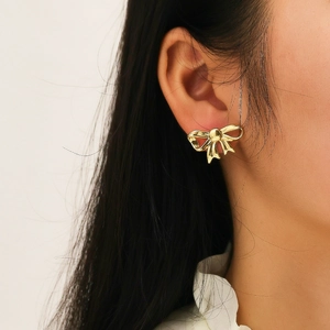 Close-up of golden bow-shaped stud earrings worn by a model in a minimalist style