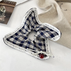 Macro detail of blue plaid scrunchie featuring white lace trim and a shiny red cherry charm