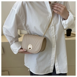 Detail of light beige saddle bag featuring shell-shaped metal lock and gold chain strap
