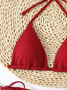 Close-up of dark red ribbed bikini top with triangle cups on a summer straw mat background