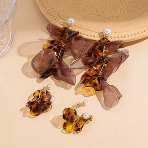 Brown amber acrylic petal drop earrings with white pearls on a textured beige plate