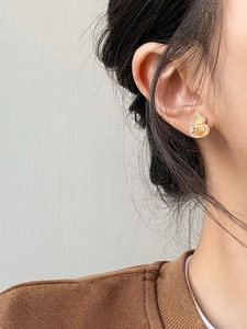 Macro detail of gold plated gourd stud earrings with yellow crystals on a model's ear