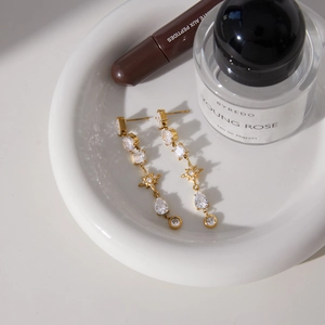Detail of gold tassel earrings with teardrop zircon on a white ceramic tray