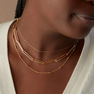 Three-layer gold layered necklace with beads and paperclip chain links on a model
