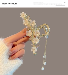 Detail of gold floral shark hair clip with white petals, rhinestones and tassel