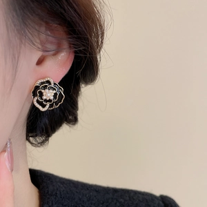 Detailed close-up of a black camellia flower earring with white pearls on a model ear