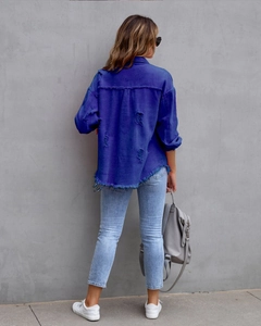 Detailansicht der Rückseite einer indigoblauen Jeansjacke mit ausgefranstem Saum und Rissen