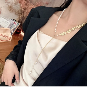 Dettaglio di una lunga collana a Y con perle naturali e fiori dorati su un abito nero