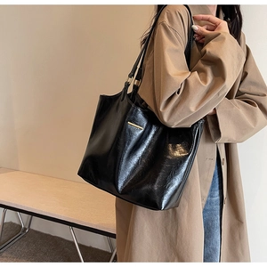 Minimalist black tote bag in glossy leather worn with a trench coat for a stylish look