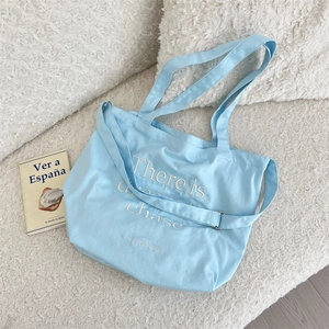 Detail of light blue canvas tote bag showing high-quality embroidery and adjustable strap