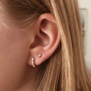 Detail of minimalist gold-plated ear cuff with rectangular zircon and small stud on ear