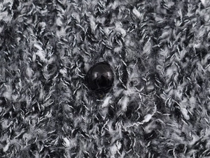 Gros plan sur la maille texturée et le bouton noir brillant d'un gilet à manches courtes