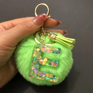 Detail of green faux fur pompom keychain with resin letter E and heart sequins