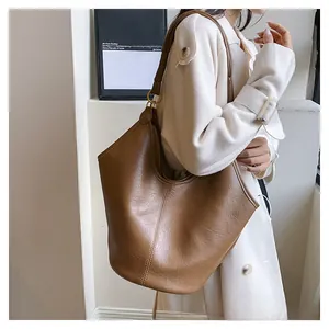 Detailed close-up of brown matte leather tote bag with wide strap and golden metal ring