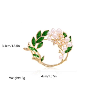 Macro detail of a gold wreath brooch with green leaves and pearls showing size measurements