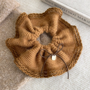 Detailed texture of brown knit scrunchie with a delicate bow and gold metal tag