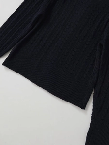 Dettaglio della classica trama a trecce e polsini a coste di un cardigan nero in lana