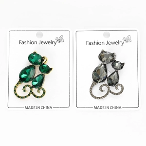 Detail view of crystal-encrusted cat brooches in green and smoky grey on a card