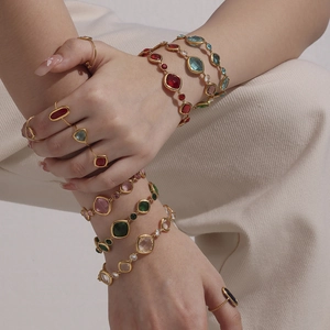 Elegantes Set aus goldfarbenen Armbändern und Ringen mit bunten Glassteinen an Modellen
