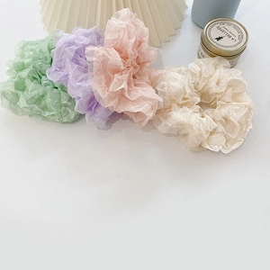 Close-up of four lace scrunchies in green purple pink and beige on a white desk
