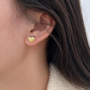 Macro shot of a gold heart bow earring featuring a 3D ribbon design and mirror finish