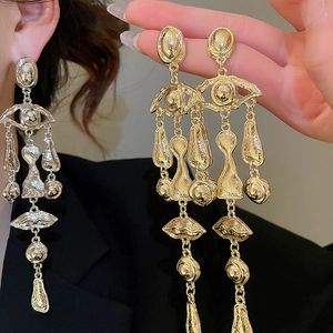 Detail of surrealist gold tassel earrings with eye and lip charms on textured metal