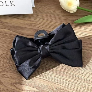 Détail d'une pince à cheveux à double nœud en satin noir sur une table en bois rustique
