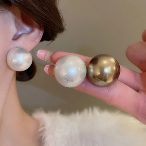 Détail de grandes boucles d'oreilles perles rondes blanches et dorées portées sur l'oreille