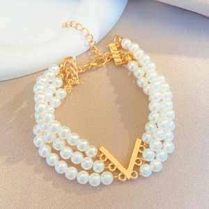 Détail d'un collier de perles multicouches avec un pendentif doré en V sur tissu