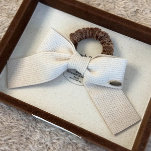 Detail of cream knit bow scrunchie with brown velvet trim in a wooden jewelry box