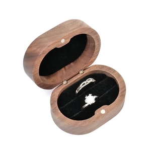 Macro shot of oval walnut wood ring box featuring black flocking lining and two silver rings
