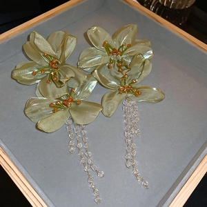 Detail view of sage green fabric flower earrings with beaded crystal tassels in a tray