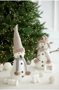 Detail of plush Christmas snowmen with knitted hats and scarves near a lit tree