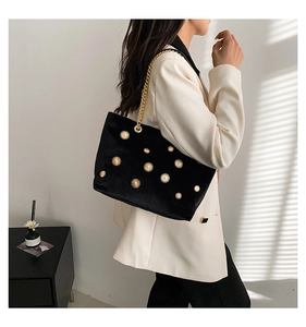 Detail of black velvet tote bag with gold sunburst rivets and elegant chain strap on a model