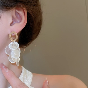 Macro detail of gold-textured hoop earrings with cascading white shell tassel discs