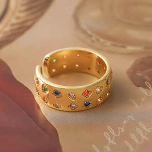Golden wide open ring with colorful star and heart zircons on polished metal surface