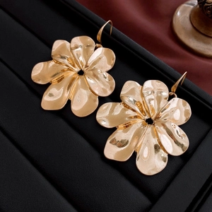 Macro shot of gold floral earrings with hammered metal texture on black display tray
