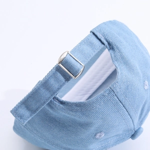 Détail de la boucle métallique et des coutures sur la casquette en jean bleu clair
