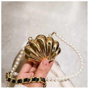 Detail of golden shell-shaped mini bag with elegant pearl chain and woven leather strap