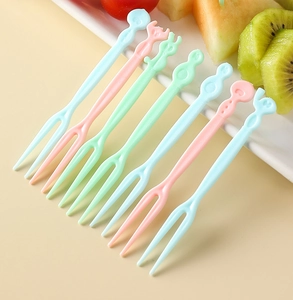 Macro detail of colorful two-prong plastic fruit forks on a white plate with fresh fruit