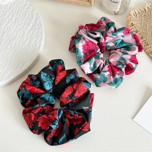 Detailed view of floral satin scrunchies with red rose prints on black and pink backgrounds