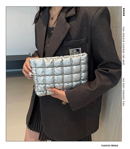 Gros plan d'une pochette matelassée argentée métallisée tenue par un mannequin élégant