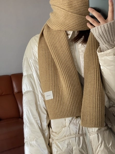 Close-up of camel knit scarf featuring a ribbed texture and white woven brand label