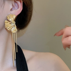 Macro view of golden ginkgo leaf earrings with long metal chain tassels worn by model