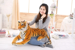Lifelike large tiger plush toy made of soft fabric being held by a model in a bedroom