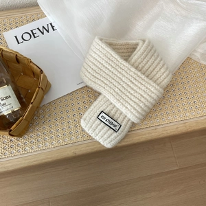 Close-up of cream knit scarf featuring a thick ribbed texture and a minimalist woven label
