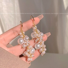 Macro view of long pearl tassel earrings featuring vertical white pearl clusters on gold hooks