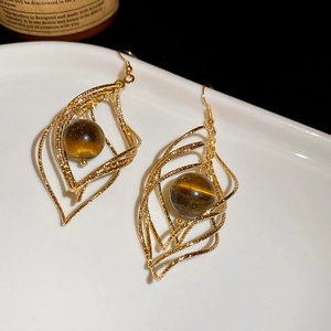 Macro shot of twisted diamond gold earrings with brown tiger eye beads on white tray